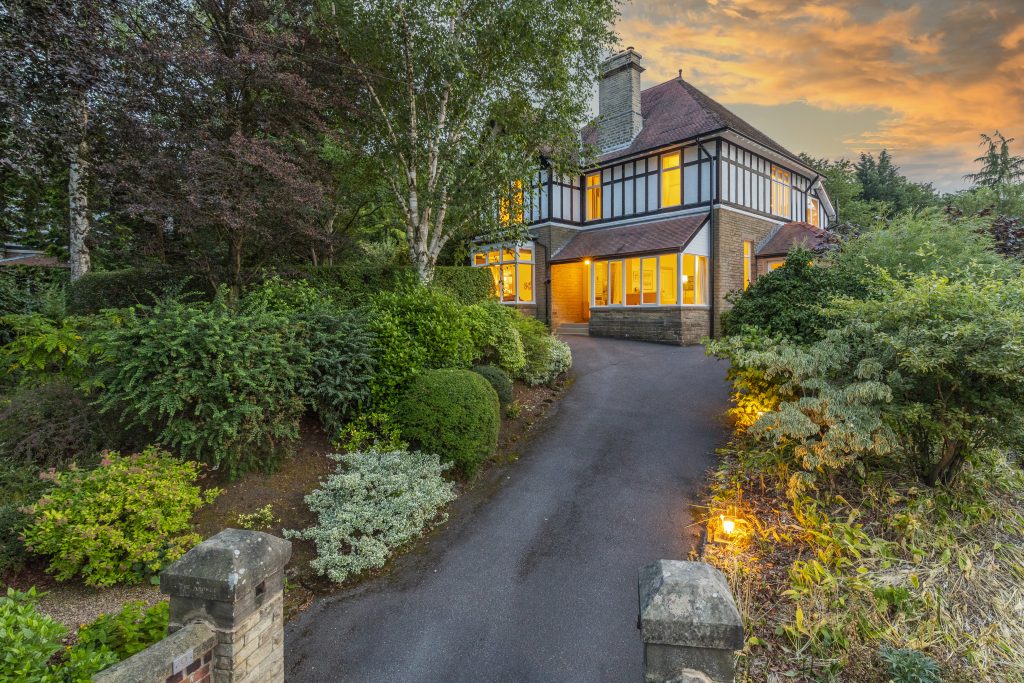 A spacious house surrounded by trees, featuring a long driveway leading up to the entrance.